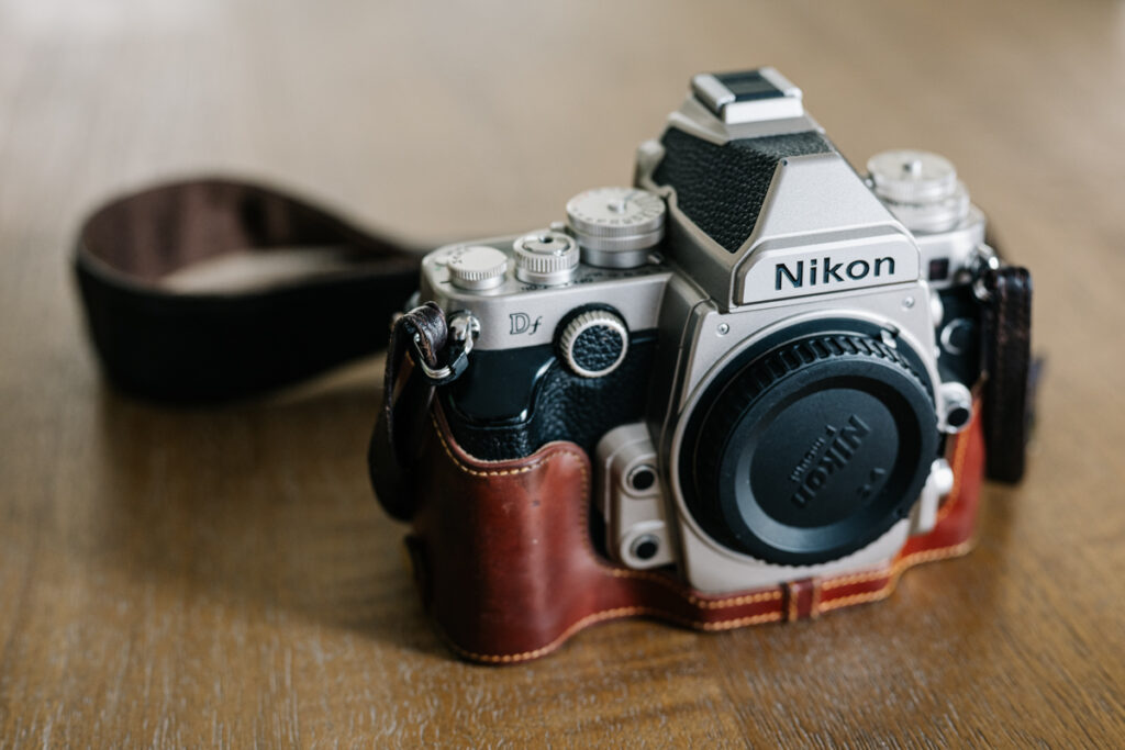 A photo of a well-used Nikon Df DSLR camera with a leather case and strap on a wooden table. 
